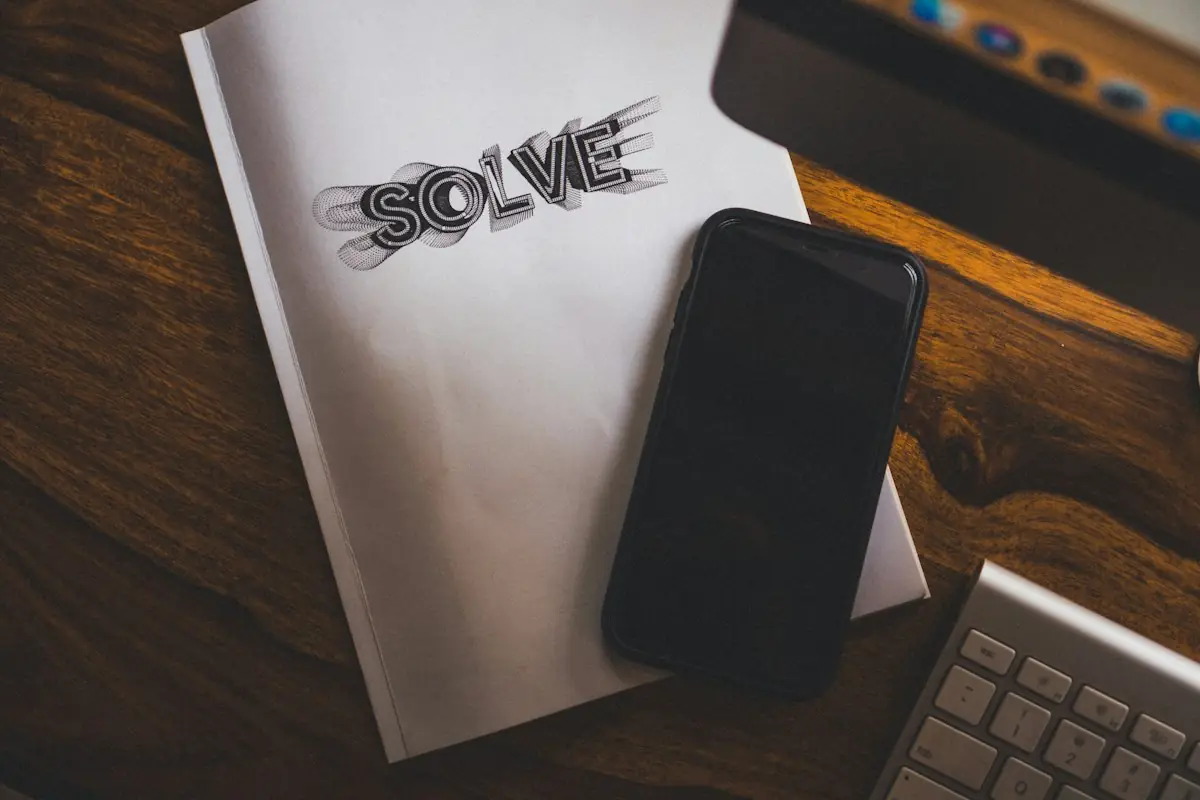 A phone lying on top of a notebook on a dark wooden table